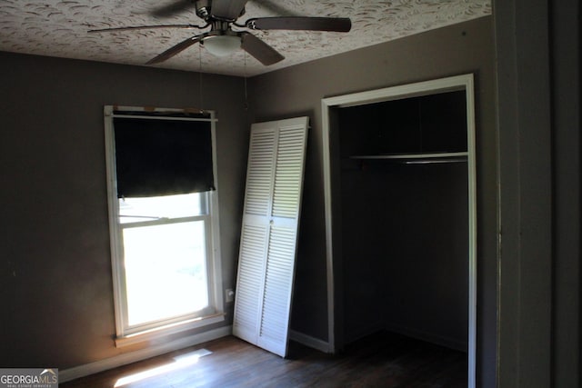 unfurnished bedroom with a textured ceiling, dark wood-type flooring, baseboards, and ceiling fan