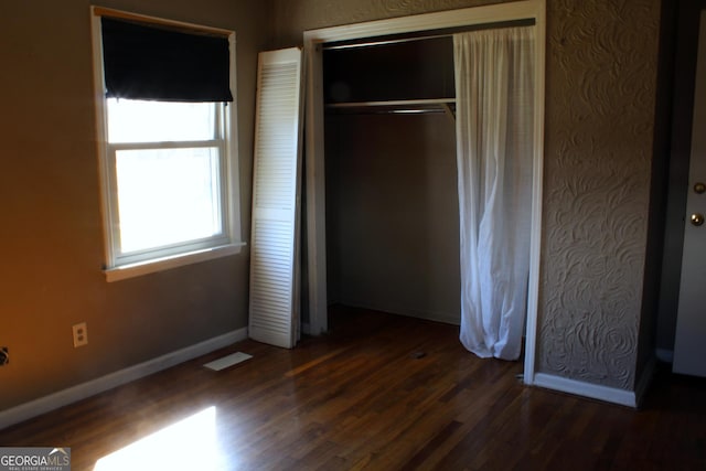 unfurnished bedroom featuring baseboards, multiple windows, a closet, and wood finished floors