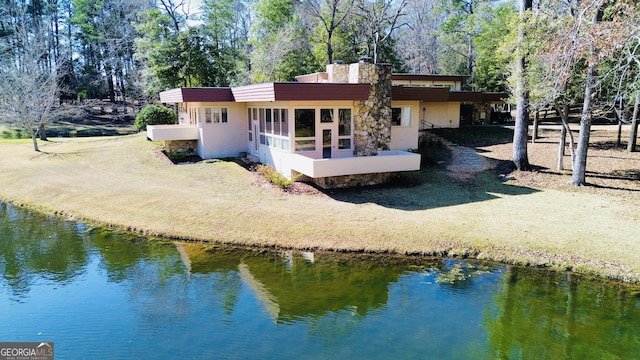 rear view of house with driveway, a chimney, and a water view