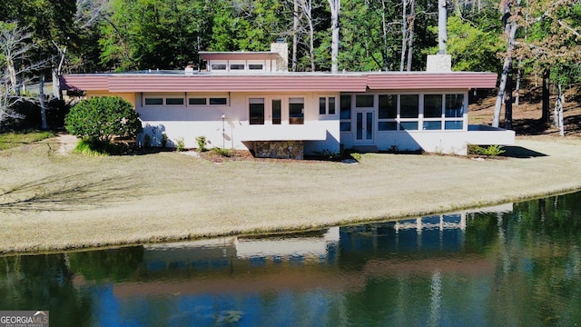 rear view of house featuring stucco siding, a water view, a chimney, and a sunroom