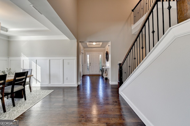 entryway with a tray ceiling, dark wood-style floors, crown molding, a decorative wall, and stairs