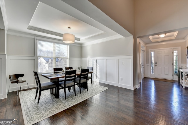 dining area with a raised ceiling, crown molding, dark wood-style flooring, and a decorative wall