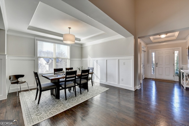 dining area with dark wood-type flooring, a decorative wall, ornamental molding, and a raised ceiling