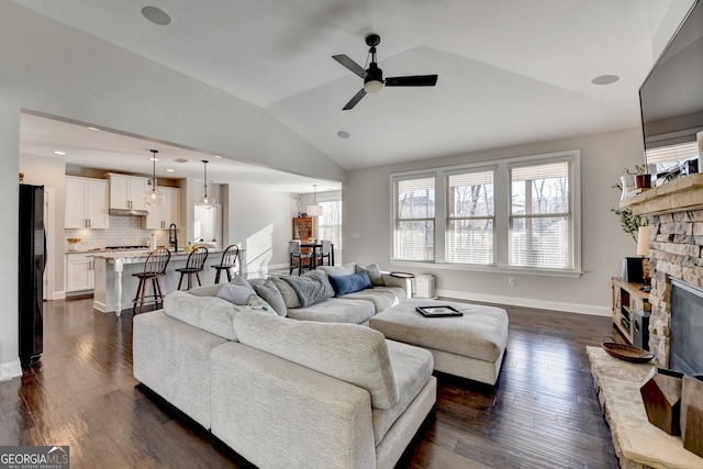 living room featuring dark wood-style floors, a fireplace, baseboards, and vaulted ceiling