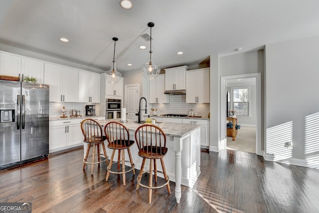 kitchen with white cabinets, visible vents, appliances with stainless steel finishes, a sink, and an island with sink