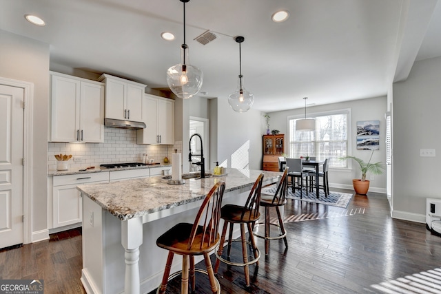 kitchen with visible vents, tasteful backsplash, light stone counters, and dark wood finished floors