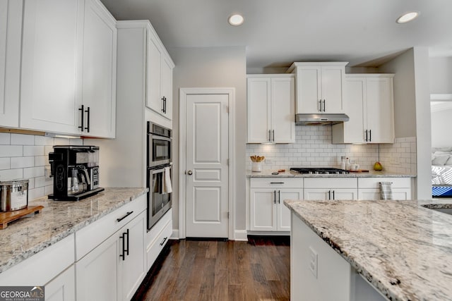 kitchen featuring under cabinet range hood, light stone counters, recessed lighting, white cabinets, and dark wood-style flooring