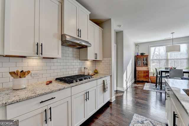 kitchen with dark wood finished floors, decorative backsplash, stainless steel gas stovetop, under cabinet range hood, and white cabinetry