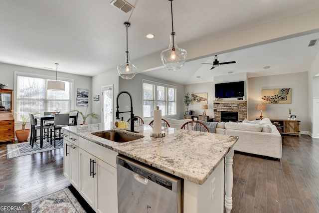 kitchen with visible vents, a sink, dishwasher, a stone fireplace, and dark wood-style flooring