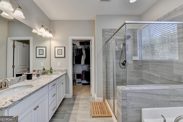 bathroom with double vanity, a spacious closet, a stall shower, and a sink