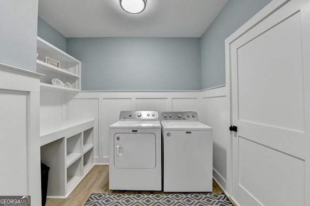 washroom with a decorative wall, a wainscoted wall, light wood-style flooring, washer and dryer, and laundry area