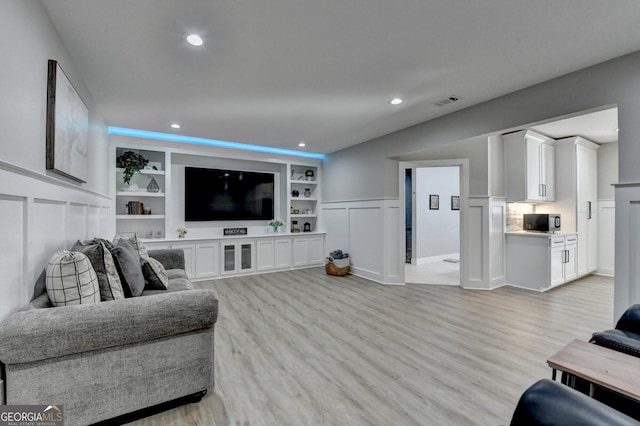 living area with a decorative wall, built in shelves, recessed lighting, and light wood-type flooring
