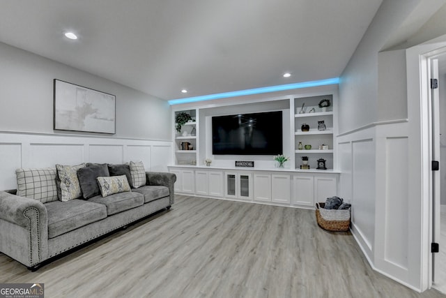 living area with built in shelves, light wood-style flooring, wainscoting, and a decorative wall