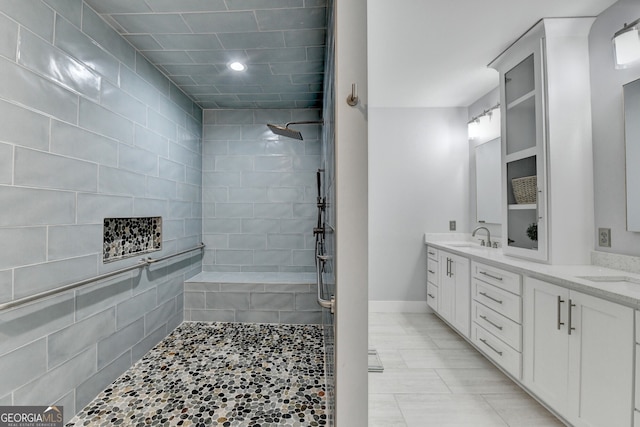 full bath featuring a sink, baseboards, double vanity, and a tile shower