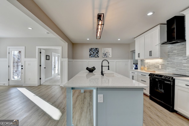 kitchen with black electric range oven, a sink, tasteful backsplash, light wood-style floors, and wall chimney exhaust hood