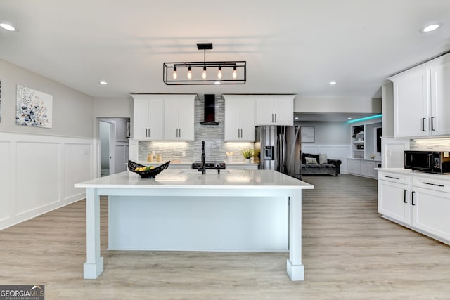 kitchen with light countertops, decorative backsplash, light wood-style floors, wall chimney range hood, and appliances with stainless steel finishes
