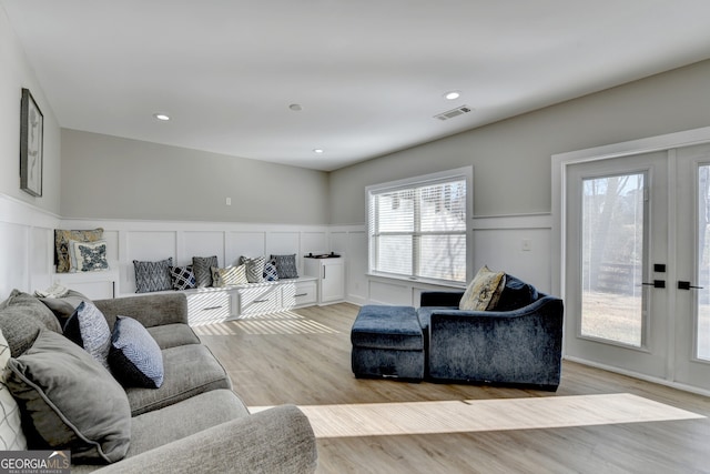 living room featuring recessed lighting, light wood finished floors, visible vents, a decorative wall, and wainscoting