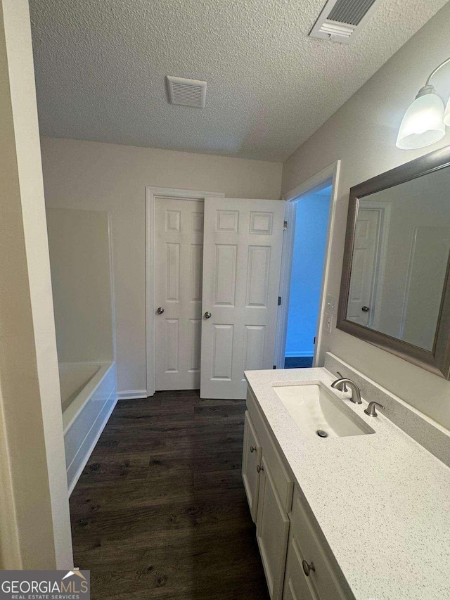 full bath featuring visible vents, a tub to relax in, a textured ceiling, wood finished floors, and vanity