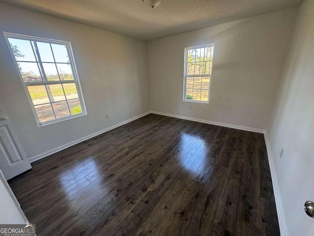 spare room featuring baseboards, dark wood-type flooring, and a textured ceiling