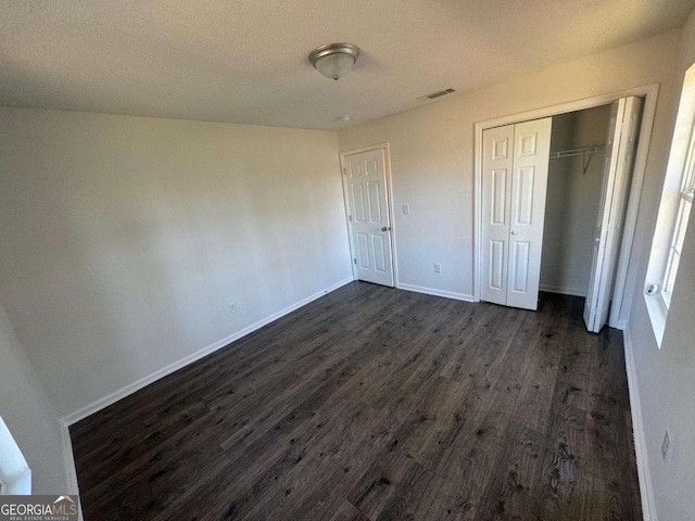 unfurnished bedroom featuring a closet, visible vents, baseboards, and dark wood-style flooring