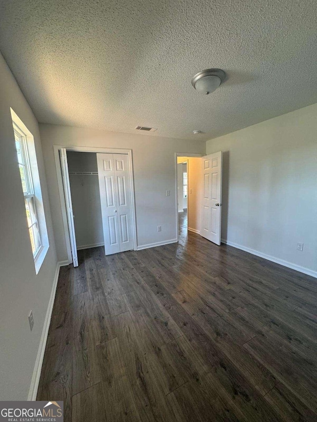 unfurnished bedroom featuring visible vents, baseboards, a closet, and dark wood-style floors