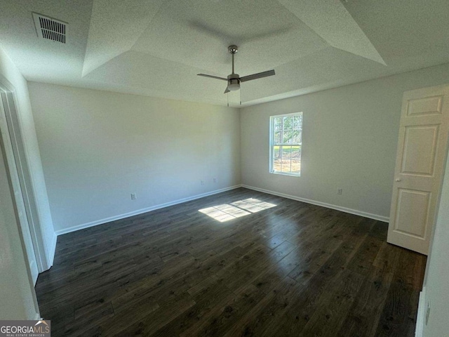 unfurnished room with visible vents, dark wood-type flooring, baseboards, a tray ceiling, and a ceiling fan