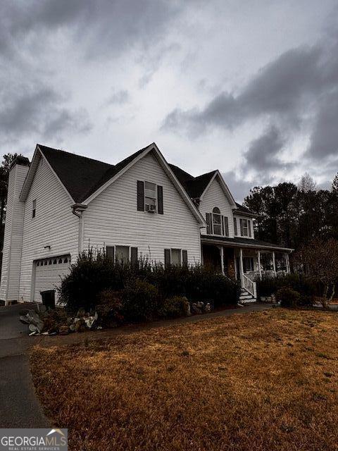 view of front of house with aphalt driveway, covered porch, a front yard, and a garage