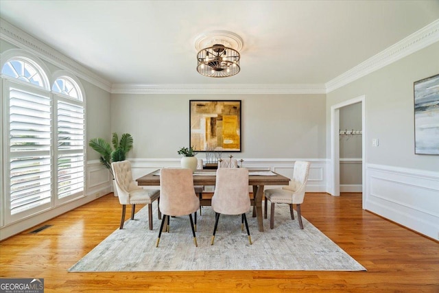 dining room with wood finished floors, visible vents, crown molding, and wainscoting