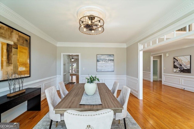 dining area featuring wainscoting, light wood-style flooring, a notable chandelier, and ornamental molding