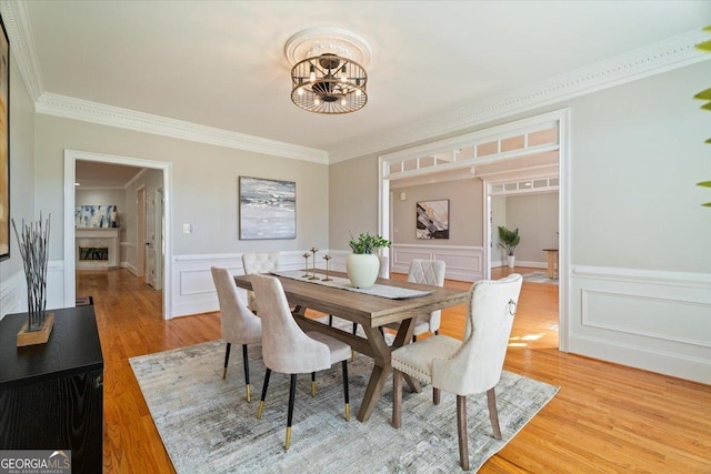 dining area featuring a chandelier, a wainscoted wall, light wood-type flooring, crown molding, and a fireplace