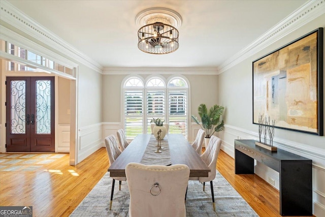 dining area featuring light wood-type flooring, ornamental molding, a notable chandelier, and french doors