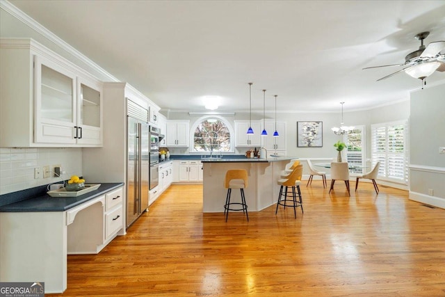 kitchen with dark countertops, a kitchen bar, light wood-type flooring, and ceiling fan with notable chandelier