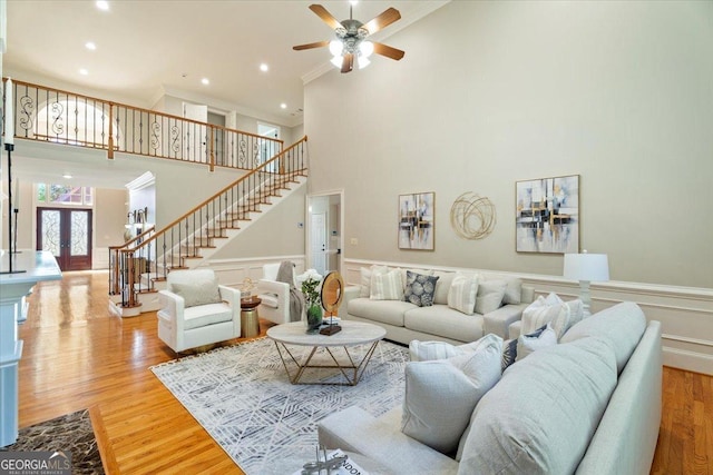 living area with stairs, light wood-type flooring, ceiling fan, a towering ceiling, and ornamental molding