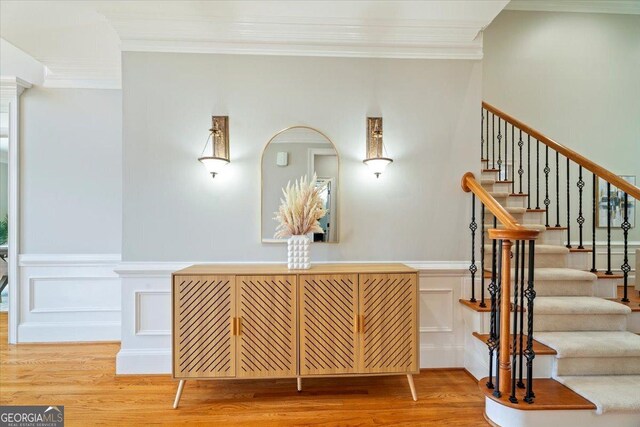staircase featuring wainscoting, a decorative wall, ornamental molding, and wood finished floors