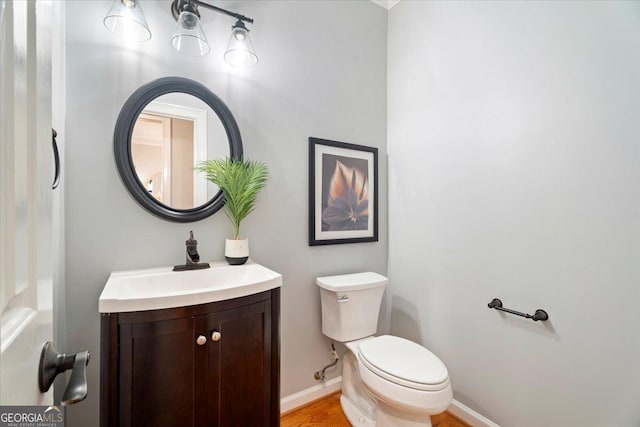 half bathroom with baseboards, toilet, vanity, and wood finished floors