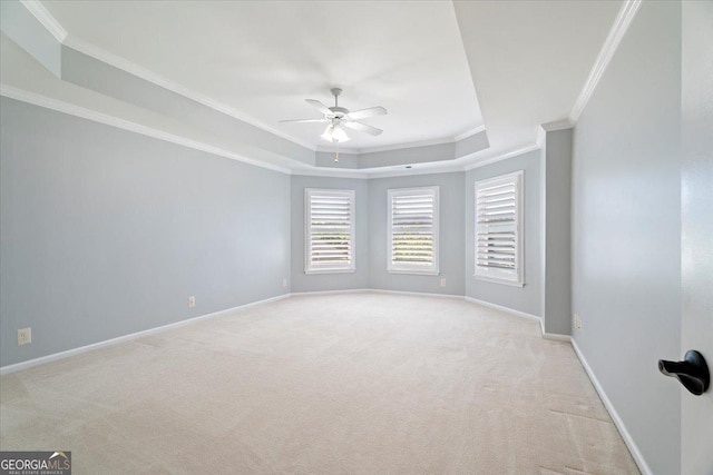 carpeted spare room with a raised ceiling, a ceiling fan, baseboards, and ornamental molding
