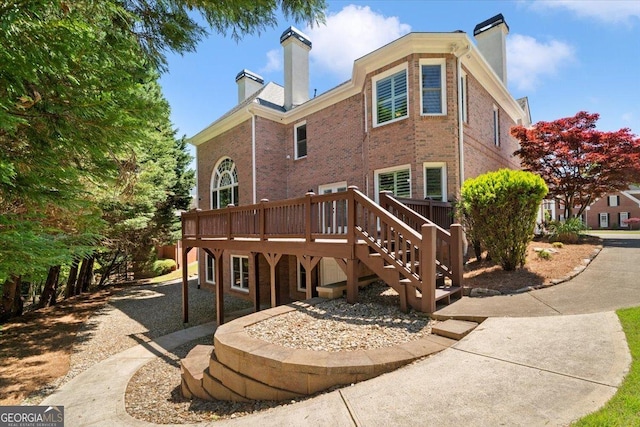 back of property featuring a chimney, brick siding, a deck, and stairway
