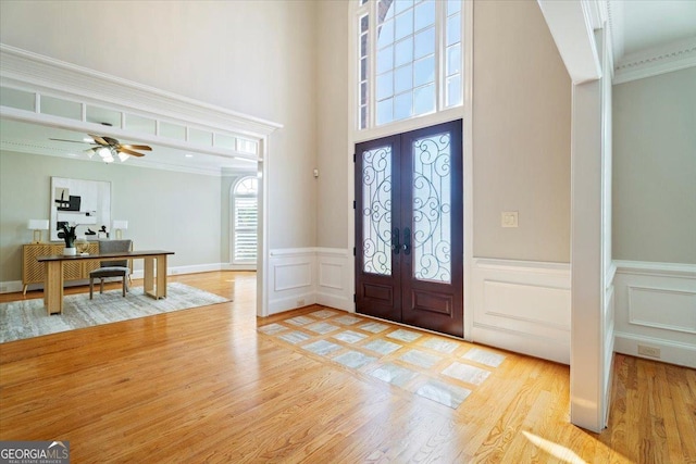 entryway featuring light wood-style flooring, french doors, a wainscoted wall, a high ceiling, and a decorative wall
