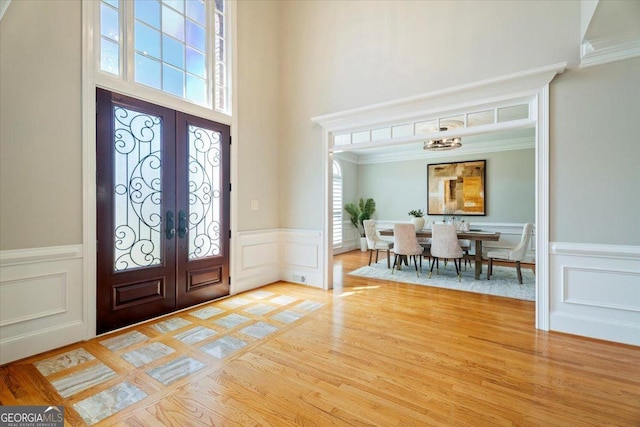 entrance foyer featuring a wainscoted wall, french doors, a towering ceiling, light wood-style floors, and a decorative wall