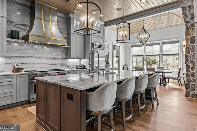 kitchen with high end stainless steel range, custom range hood, light stone counters, backsplash, and wooden ceiling