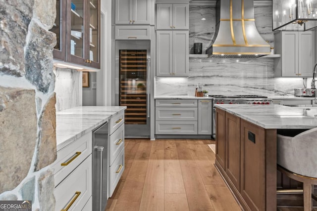 kitchen with light stone counters, gray cabinets, decorative backsplash, wall chimney exhaust hood, and light wood-type flooring
