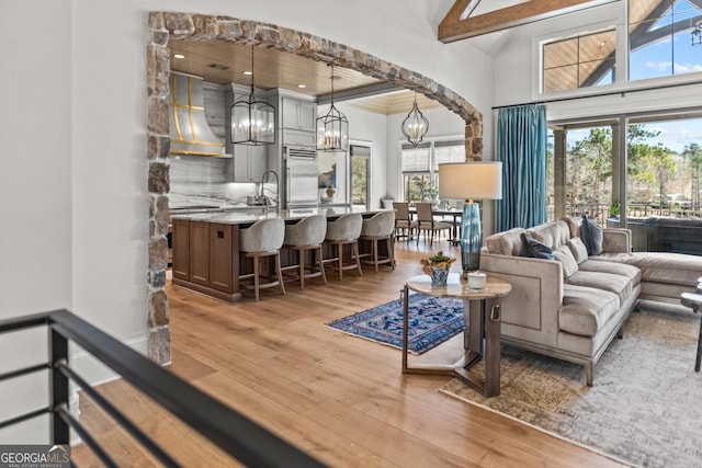 living room featuring beam ceiling, plenty of natural light, light wood-style floors, and a chandelier