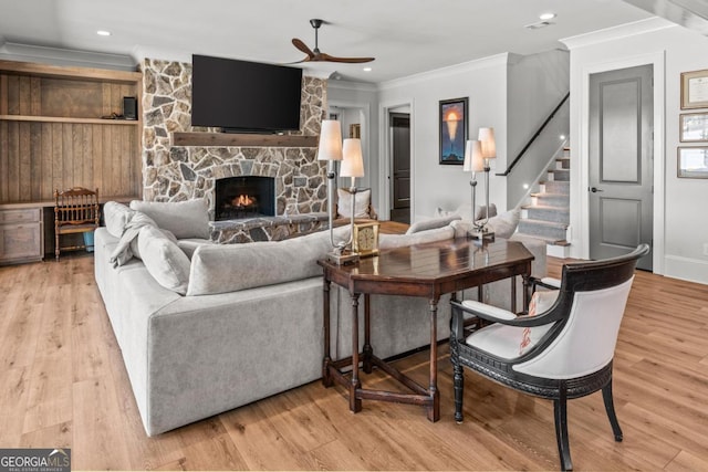 living room featuring light wood finished floors, a stone fireplace, and ornamental molding