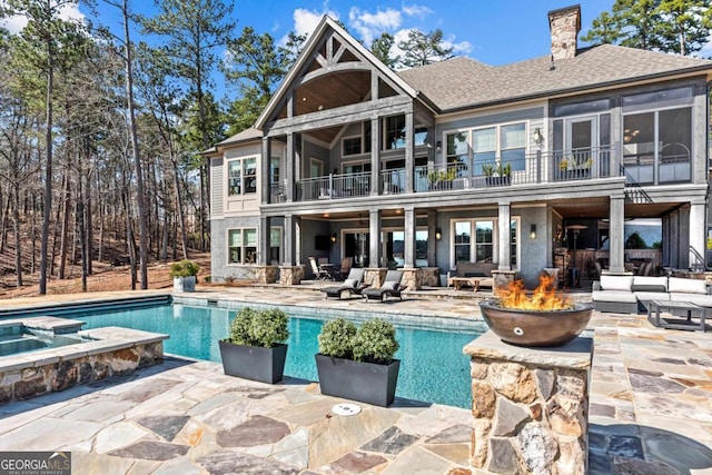 back of house featuring a pool with connected hot tub, an outdoor living space with a fire pit, a balcony, a chimney, and a patio area