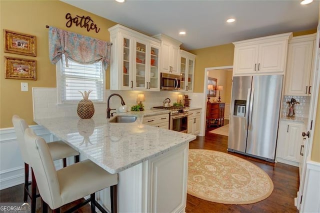 kitchen featuring a breakfast bar, light stone counters, appliances with stainless steel finishes, a peninsula, and a sink