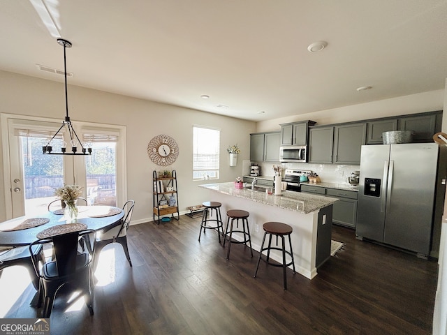 kitchen featuring an island with sink, gray cabinetry, dark wood-type flooring, appliances with stainless steel finishes, and a kitchen breakfast bar