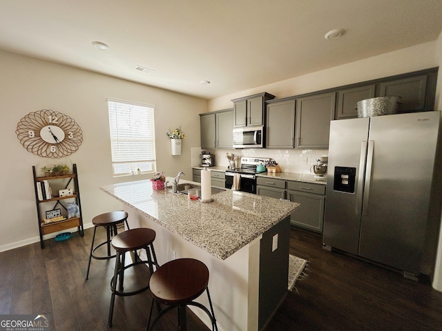 kitchen featuring dark wood finished floors, a breakfast bar, an island with sink, a sink, and appliances with stainless steel finishes