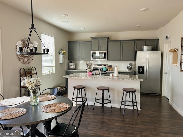 kitchen featuring a kitchen bar, a center island with sink, backsplash, dark wood-style floors, and appliances with stainless steel finishes