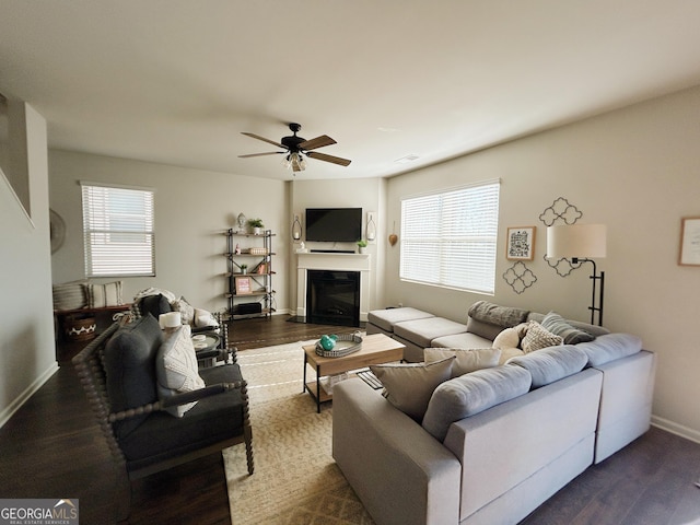 living area with a wealth of natural light, dark wood-style floors, a glass covered fireplace, and ceiling fan