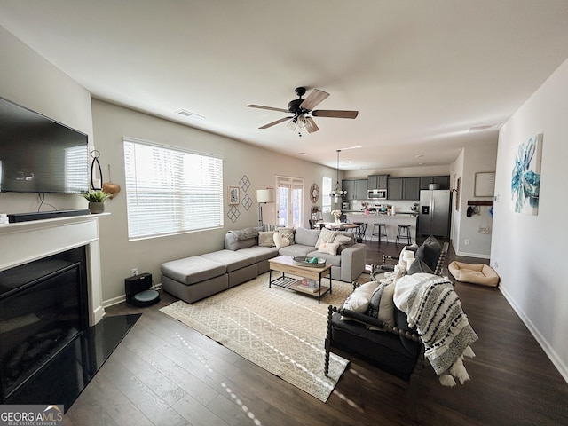 living area featuring visible vents, baseboards, dark wood-type flooring, and a ceiling fan